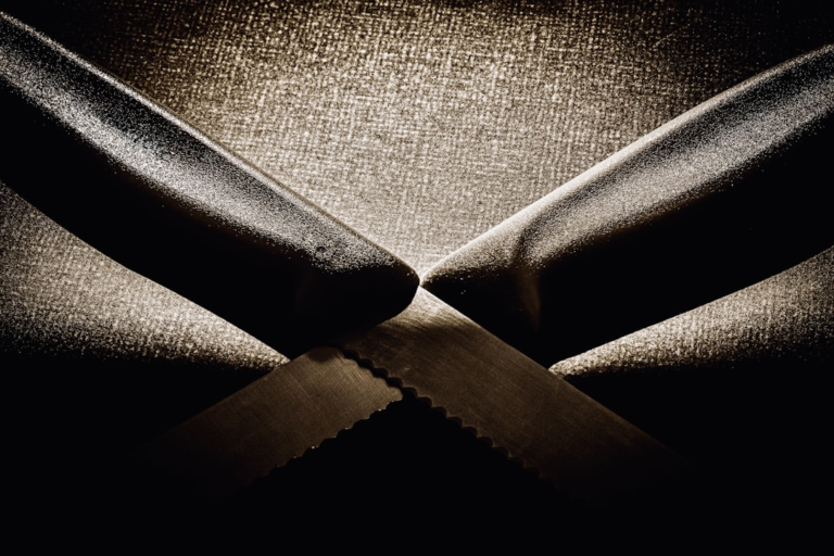 Two serrated knives crossing on a dark, textured background. — Foto por Sebastian Schuster na Unsplash