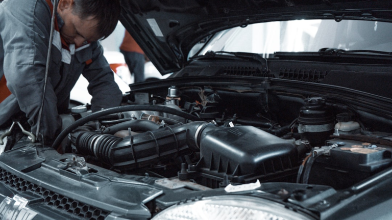 A mechanic in a grey uniform inspecting the engine of a car — Foto por Kate Ibragimova na Unsplash