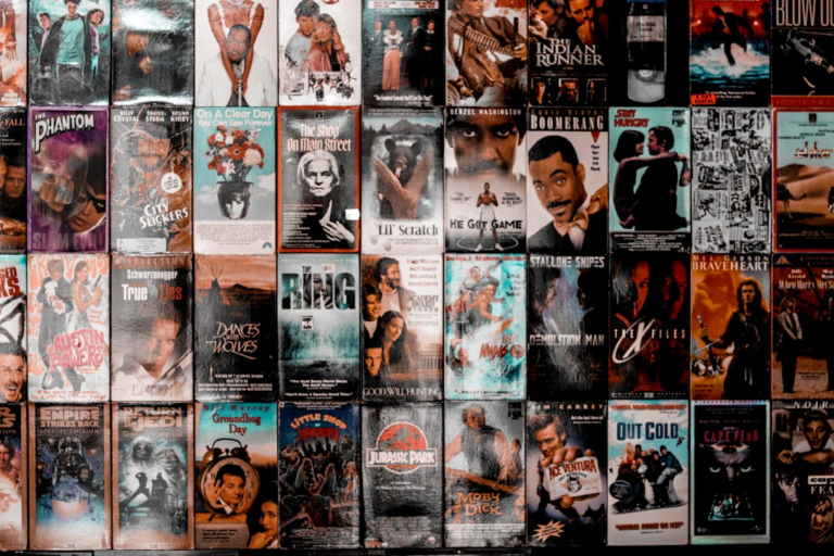 A wall covered with a grid of vintage VHS movie cassette covers — Foto por Tyson Moultrie na Unsplash